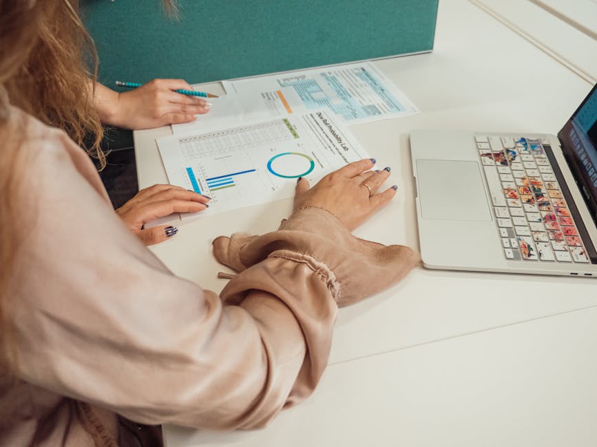 Two colleagues in discussion over data reports and laptop in modern office setting.